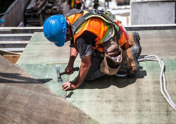 A skilled construction worker in protective gear hammering a rooftop panel.